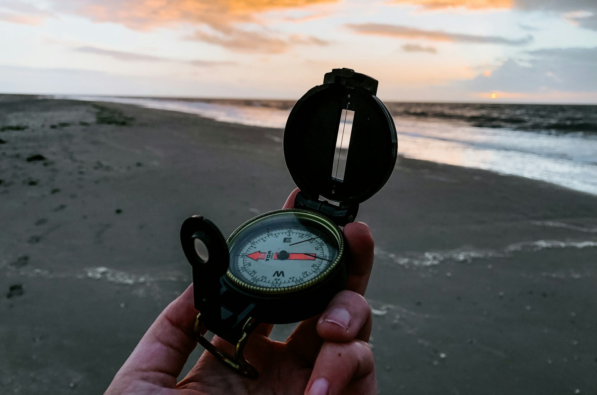 Hand houdt een kompas vast op een strand bij zonsondergang.